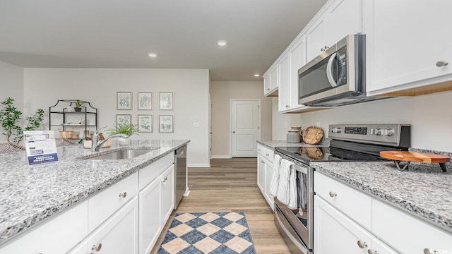 kitchen featuring appliances with stainless steel finishes, a sink, white cabinets, light wood-style flooring, and recessed lighting