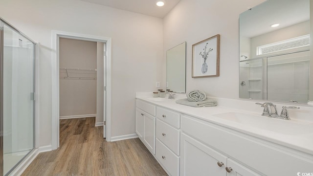 full bath featuring wood finished floors, a shower stall, a walk in closet, double vanity, and baseboards