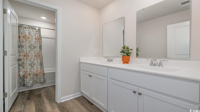 full bath with wood finished floors, double vanity, baseboards, and shower / tub combo