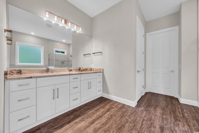 bathroom featuring a tile shower, baseboards, wood finished floors, and double vanity