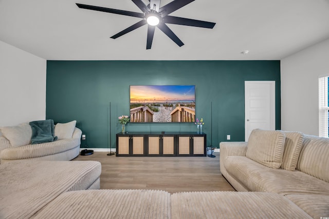 living room featuring wood finished floors, a ceiling fan, baseboards, and an accent wall