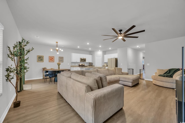 living area with light wood-style flooring, a ceiling fan, recessed lighting, baseboards, and a chandelier