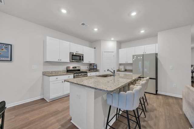 kitchen featuring stainless steel appliances, a sink, baseboards, light wood-style flooring, and recessed lighting