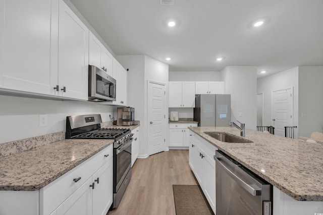 kitchen with appliances with stainless steel finishes, a sink, light wood-style flooring, an island with sink, and recessed lighting