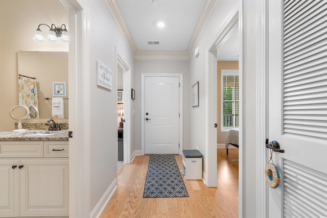 entryway featuring a sink, light wood-style flooring, ornamental molding, and baseboards