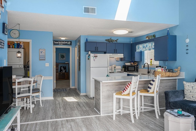 kitchen featuring black microwave, blue cabinetry, freestanding refrigerator, a peninsula, and light countertops