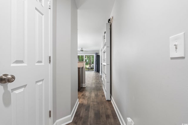 hall featuring a barn door, dark wood-style flooring, and baseboards