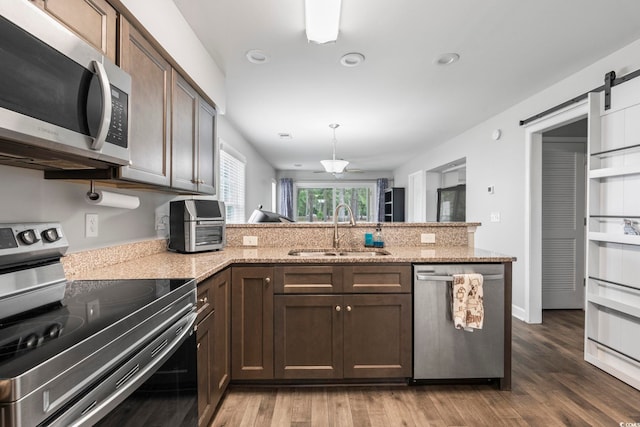 kitchen with appliances with stainless steel finishes, a sink, a peninsula, wood finished floors, and dark brown cabinetry