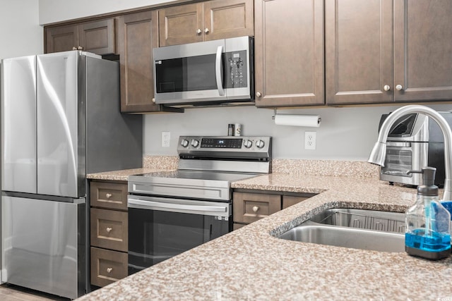 kitchen featuring stainless steel appliances, a sink, dark brown cabinets, and light stone counters