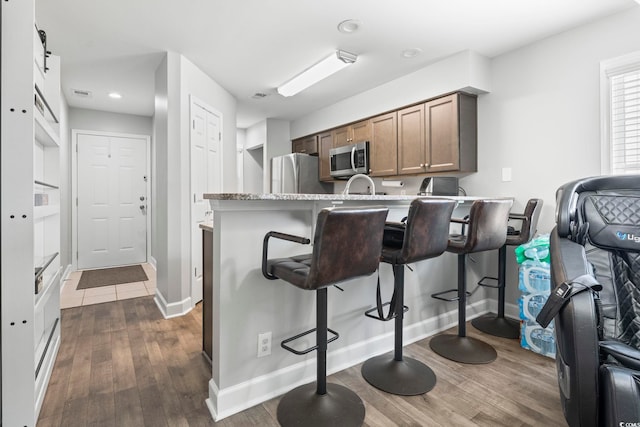 kitchen with stainless steel appliances, a kitchen breakfast bar, dark wood-style floors, baseboards, and a peninsula