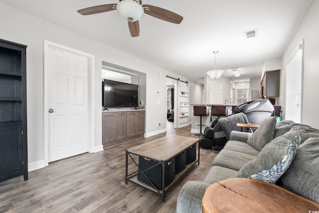 living room with a barn door, ceiling fan, wood finished floors, and baseboards