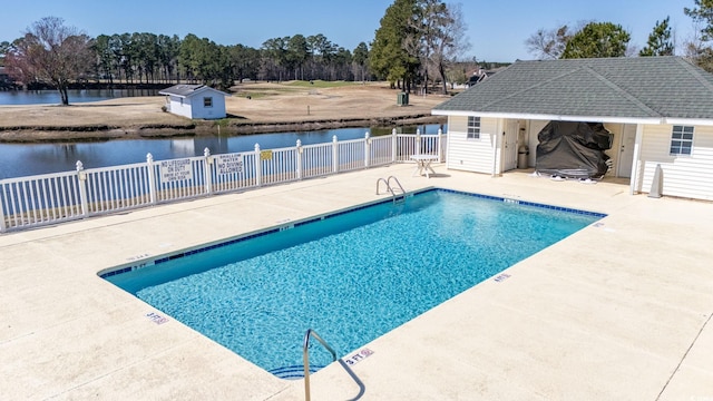 community pool with a patio, a water view, an outbuilding, and fence