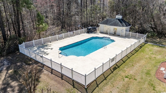view of pool featuring a patio area, a wooded view, and an outbuilding
