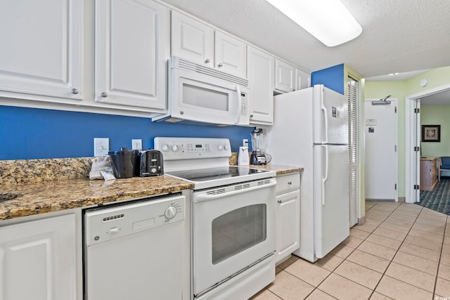 kitchen featuring white appliances, white cabinetry, light tile patterned floors, a textured ceiling, and dark stone counters
