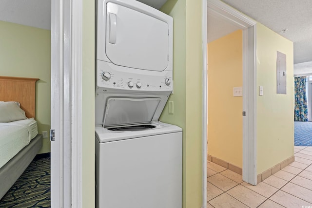 laundry room with stacked washing machine and dryer, light tile patterned floors, electric panel, and baseboards