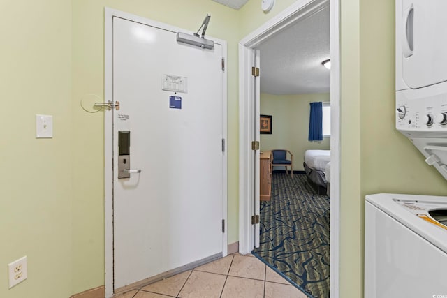 washroom featuring stacked washer / drying machine, a textured ceiling, light tile patterned flooring, and baseboards