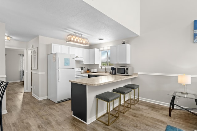 1891 Colony Dr Unit 15J, Surfside Beach, SC 29575 - kitchen with white appliances, a peninsula, a breakfast bar, light wood-style flooring, and white cabinets
