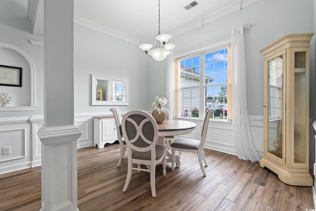 dining area with a chandelier, ornamental molding, a wainscoted wall, wood finished floors, and a decorative wall