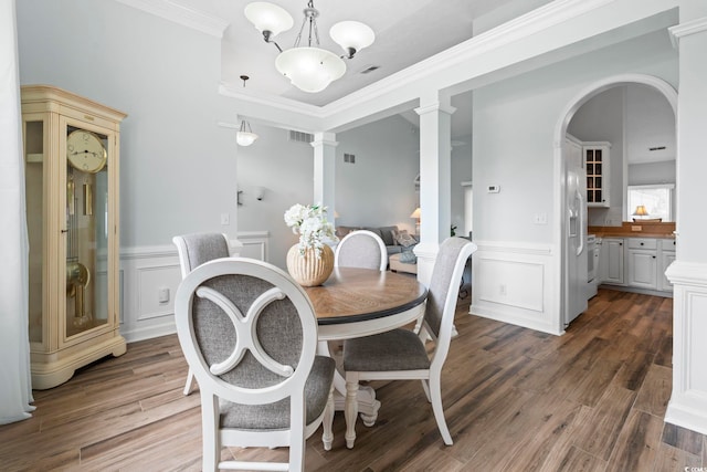dining room featuring decorative columns, wainscoting, wood finished floors, crown molding, and a decorative wall