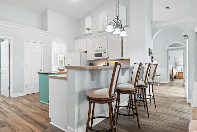 kitchen featuring white appliances, arched walkways, a towering ceiling, a breakfast bar area, and wood finished floors