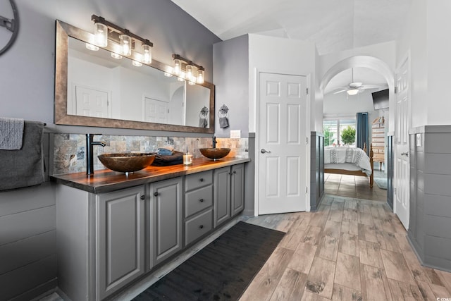 ensuite bathroom with ceiling fan, tasteful backsplash, double vanity, and wood finished floors