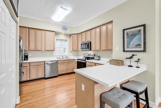 kitchen with stainless steel appliances, a peninsula, a breakfast bar area, light brown cabinetry, and a textured ceiling