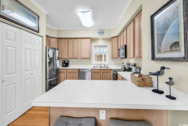 kitchen featuring appliances with stainless steel finishes, a peninsula, a breakfast bar area, a sink, and a textured ceiling