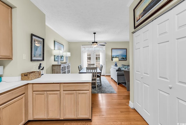 kitchen with a peninsula, crown molding, light wood finished floors, a ceiling fan, and light countertops