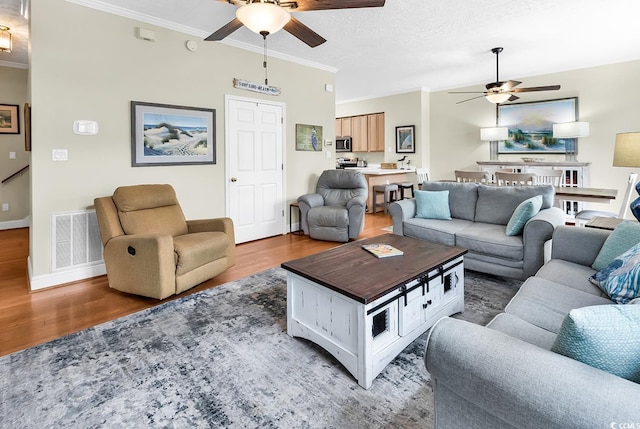living area with a ceiling fan, wood finished floors, ornamental molding, and baseboards