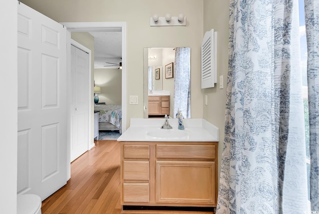 ensuite bathroom featuring wood finished floors, vanity, ceiling fan, and curtained shower