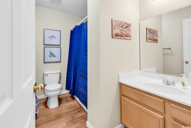 bathroom with wood finished floors, toilet, vanity, baseboards, and a textured ceiling