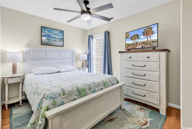bedroom with wood finished floors, a textured ceiling, baseboards, and ceiling fan