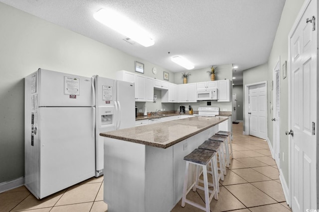 kitchen featuring white appliances, light tile patterned floors, white cabinets, dark stone counters, and a textured ceiling