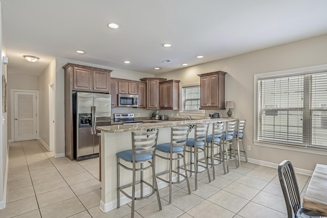 703 37th Ave S, North Myrtle Beach, SC 29582 - kitchen with stainless steel appliances, light tile patterned floors, a peninsula, a kitchen bar, and baseboards
