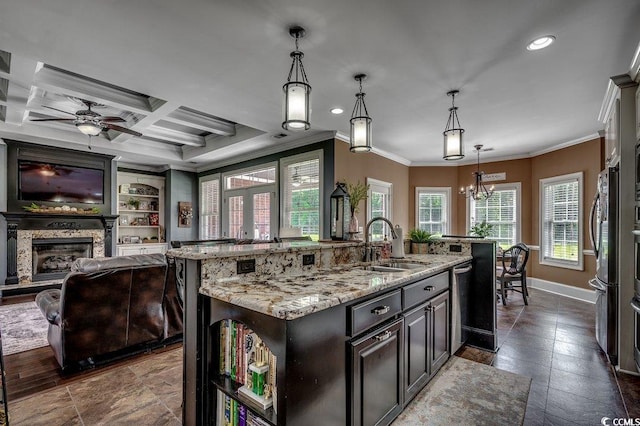 kitchen featuring a sink, a fireplace with raised hearth, crown molding, an island with sink, and light stone counters
