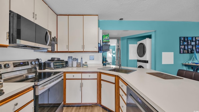 kitchen with stainless steel appliances, stacked washing machine and dryer, a sink, light countertops, and a textured ceiling