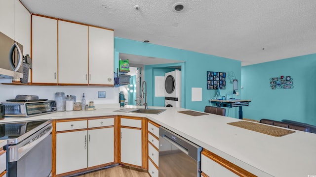 kitchen with a sink, appliances with stainless steel finishes, stacked washer / dryer, light countertops, and a textured ceiling