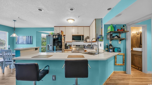 kitchen with stainless steel appliances, a peninsula, a textured ceiling, light countertops, and light wood-type flooring
