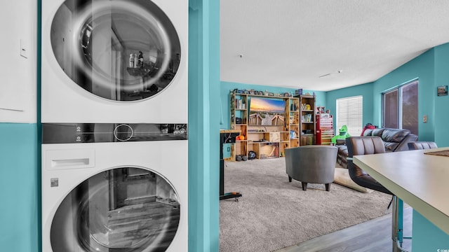 clothes washing area featuring stacked washing machine and dryer, a textured ceiling, and wood finished floors