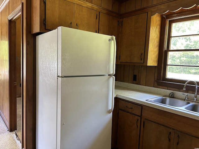kitchen with freestanding refrigerator, a sink, plenty of natural light, light countertops, and wood walls