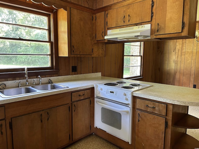 kitchen featuring white electric stove, under cabinet range hood, a sink, light countertops, and wood walls