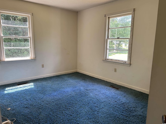 unfurnished room with dark carpet, healthy amount of natural light, baseboards, and a textured ceiling