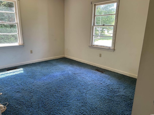 spare room with healthy amount of natural light, baseboards, and dark carpet