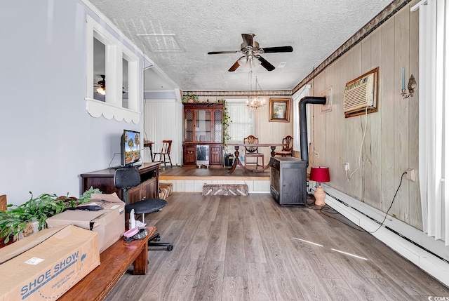 living room featuring a baseboard heating unit, wood finished floors, a wood stove, ceiling fan, and crown molding