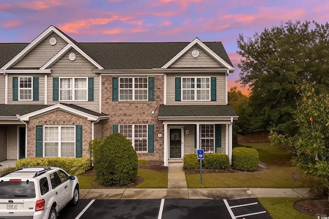 view of property with uncovered parking, brick siding, a front lawn, and a shingled roof