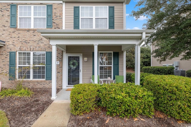 doorway to property featuring a porch, cooling unit, and brick siding
