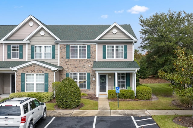 view of property with uncovered parking, brick siding, a shingled roof, and a front yard