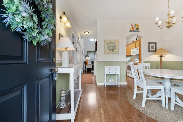 foyer entrance featuring a chandelier, wood finished floors, a wainscoted wall, and arched walkways