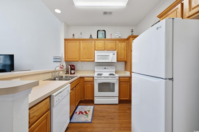 kitchen featuring white appliances, a sink, light wood finished floors, a peninsula, and light countertops