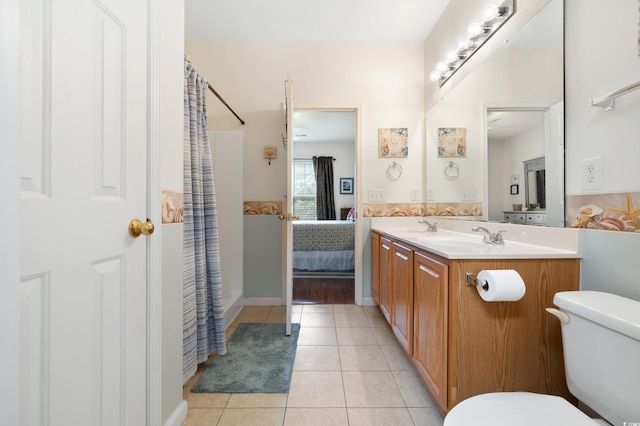 ensuite bathroom featuring toilet, tile patterned floors, double vanity, and curtained shower